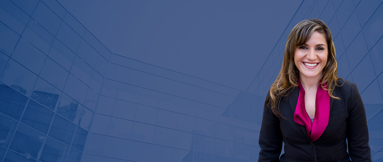 Photo of Rina Feld standing in front of a modern building with a reflective glass facade under a clear sky.